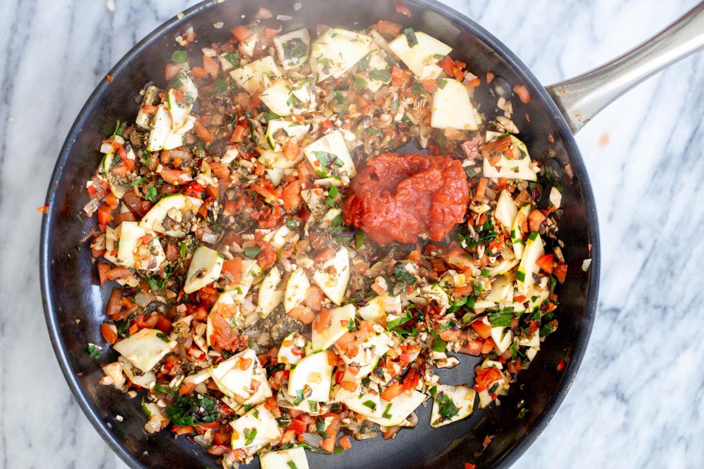 tomato paste being added to a sauteeing pan with veggies