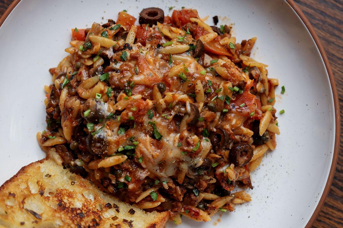 orzo puttanesca on a plate with garlic bread