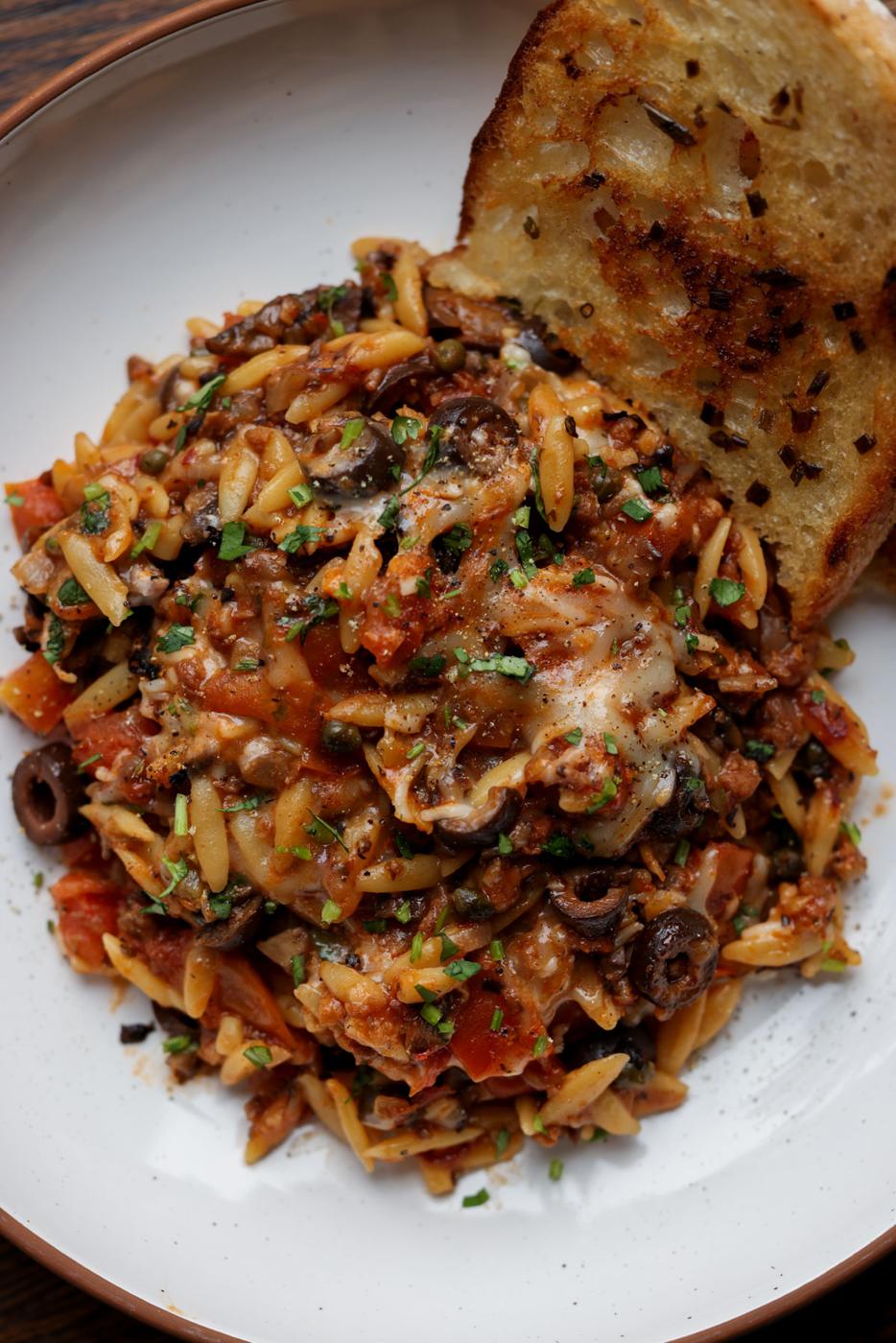 orzo puttanesca on a plate with garlic bread