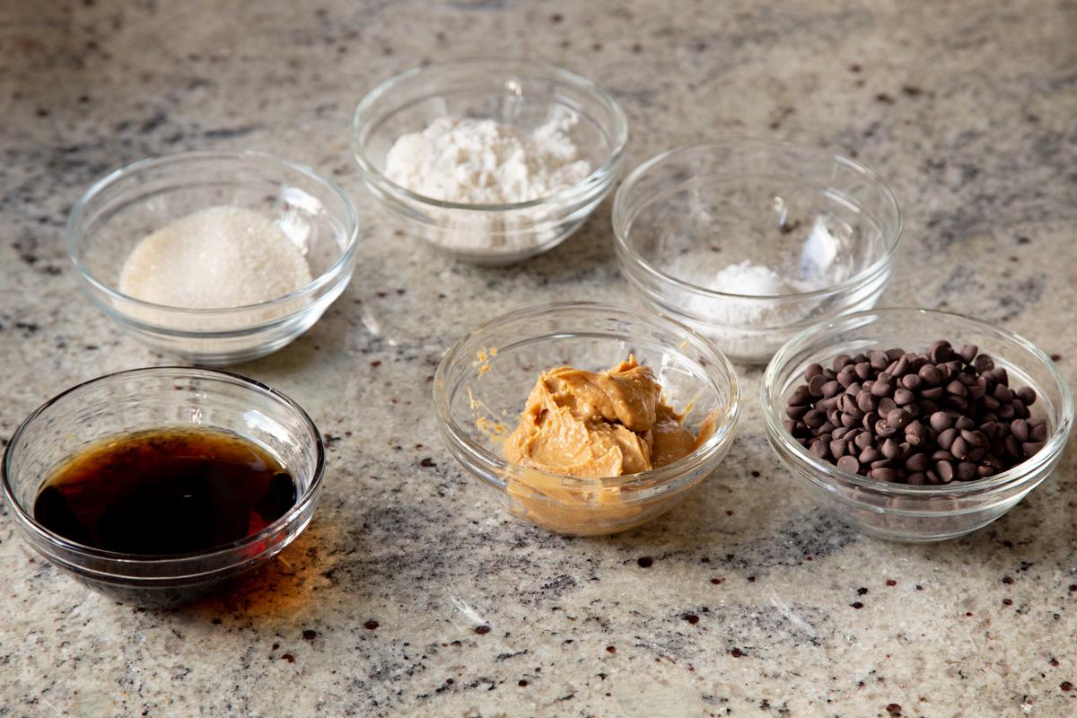 peanut butter, flour, and other cookie ingredients in small bowls on a kitchen counter
