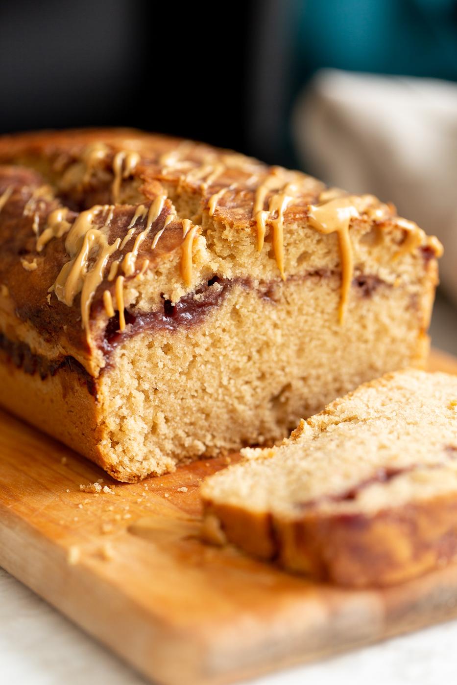 close up of a sliced vegan pb and j loaf cake drizzled with peanut butter on a cutting board