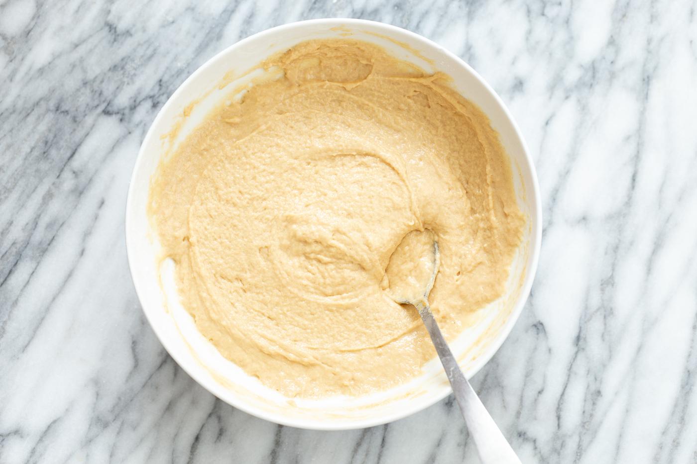 peanut butter cake batter being mixed with a metal spoon in a white mixing bowl