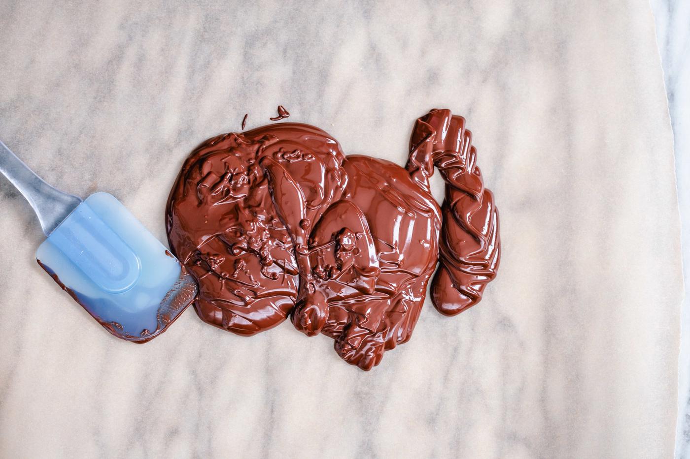 dark melted vegan chocolate being spread out on a sheet of parchment paper to make bark