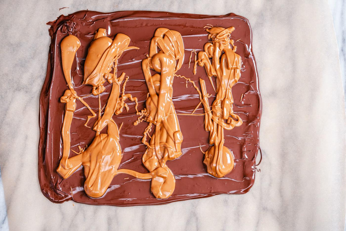 melted peanut butter being spread on top of melted chocolate to make bark