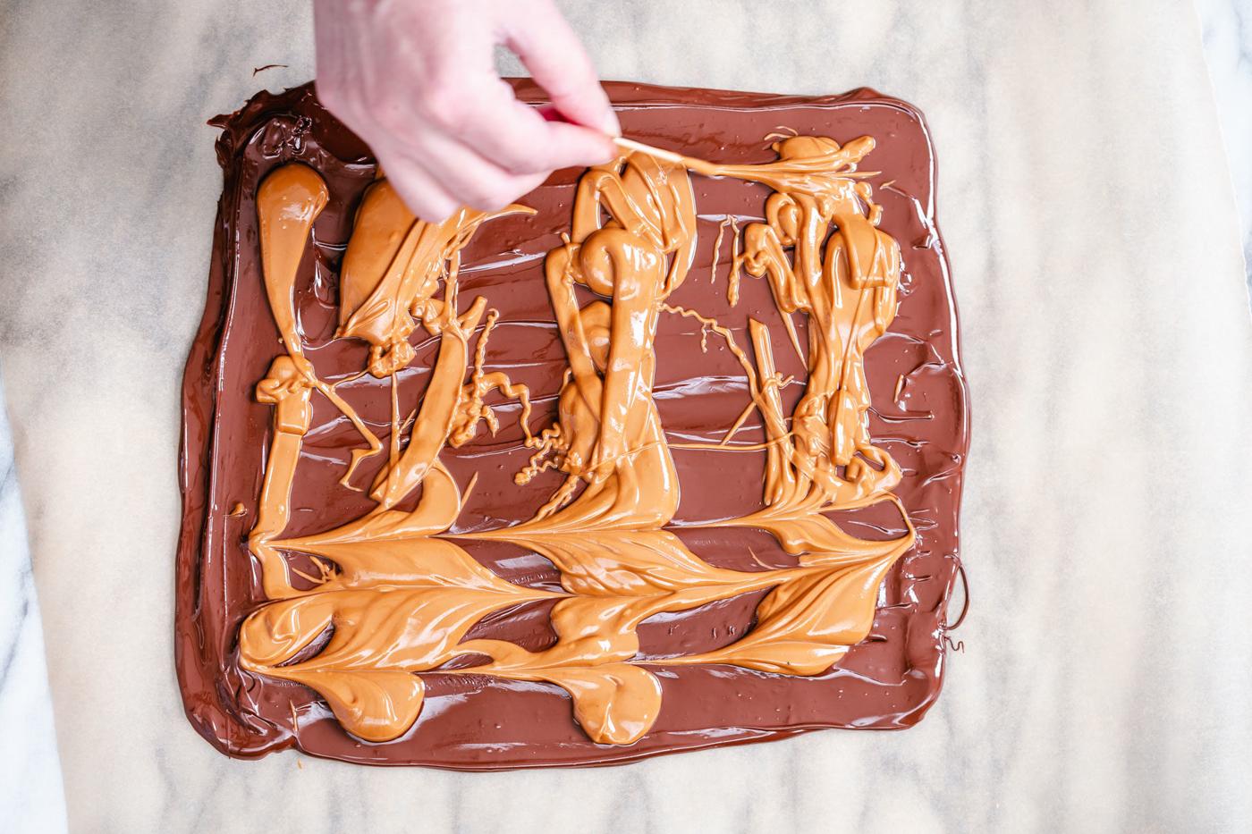 melted peanut butter being swirled into a rectangle of melted chocolate to make chocolate bark