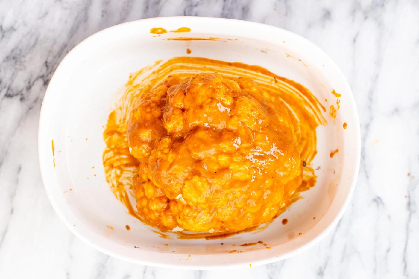 a miso peanut butter glazed head of cauliflower in a white casserole dish