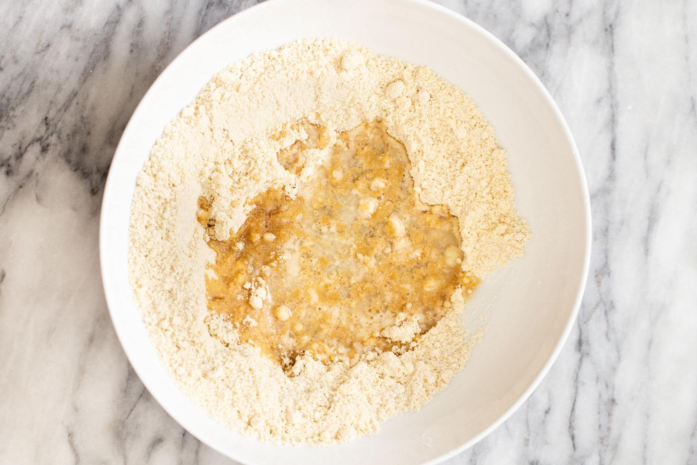 coconut oil being added to dry mix to make base for vegan pecan pie bars