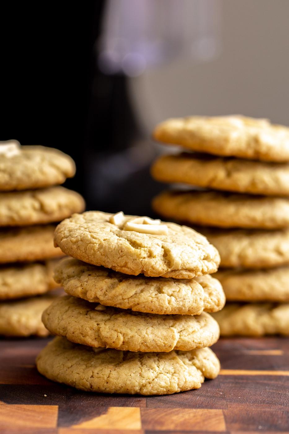 stacked vegan pistachio cookies topped with slivered almonds on a wooden chopping board