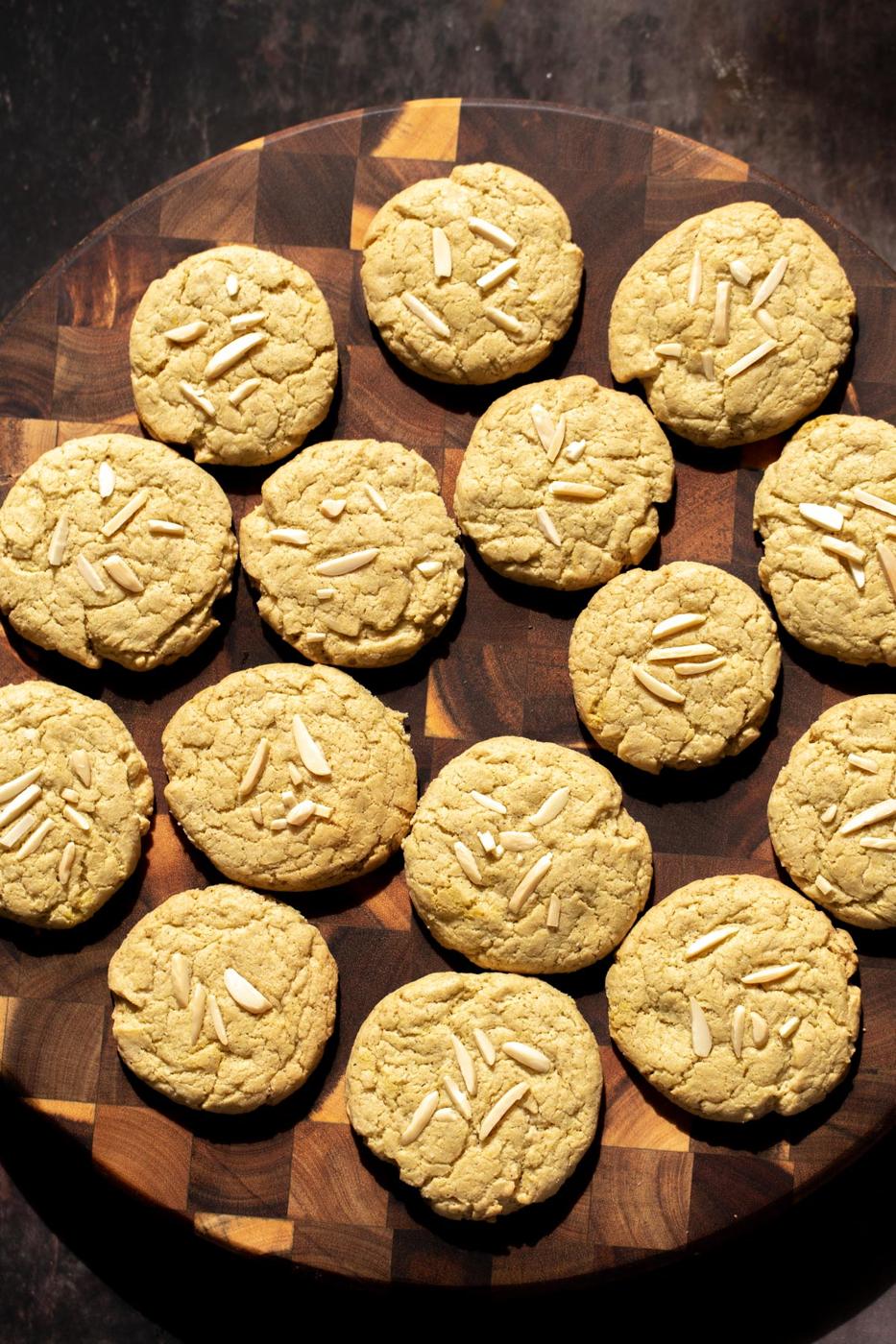 vegan pistachio cookies decorated with almond slivers on a wooden board