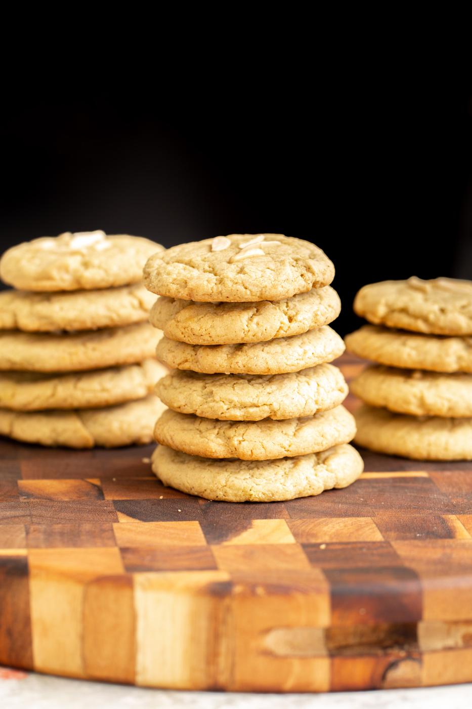 stacked vegan almond flour pistachio cookies topped with slivered almonds on a wooden chopping board