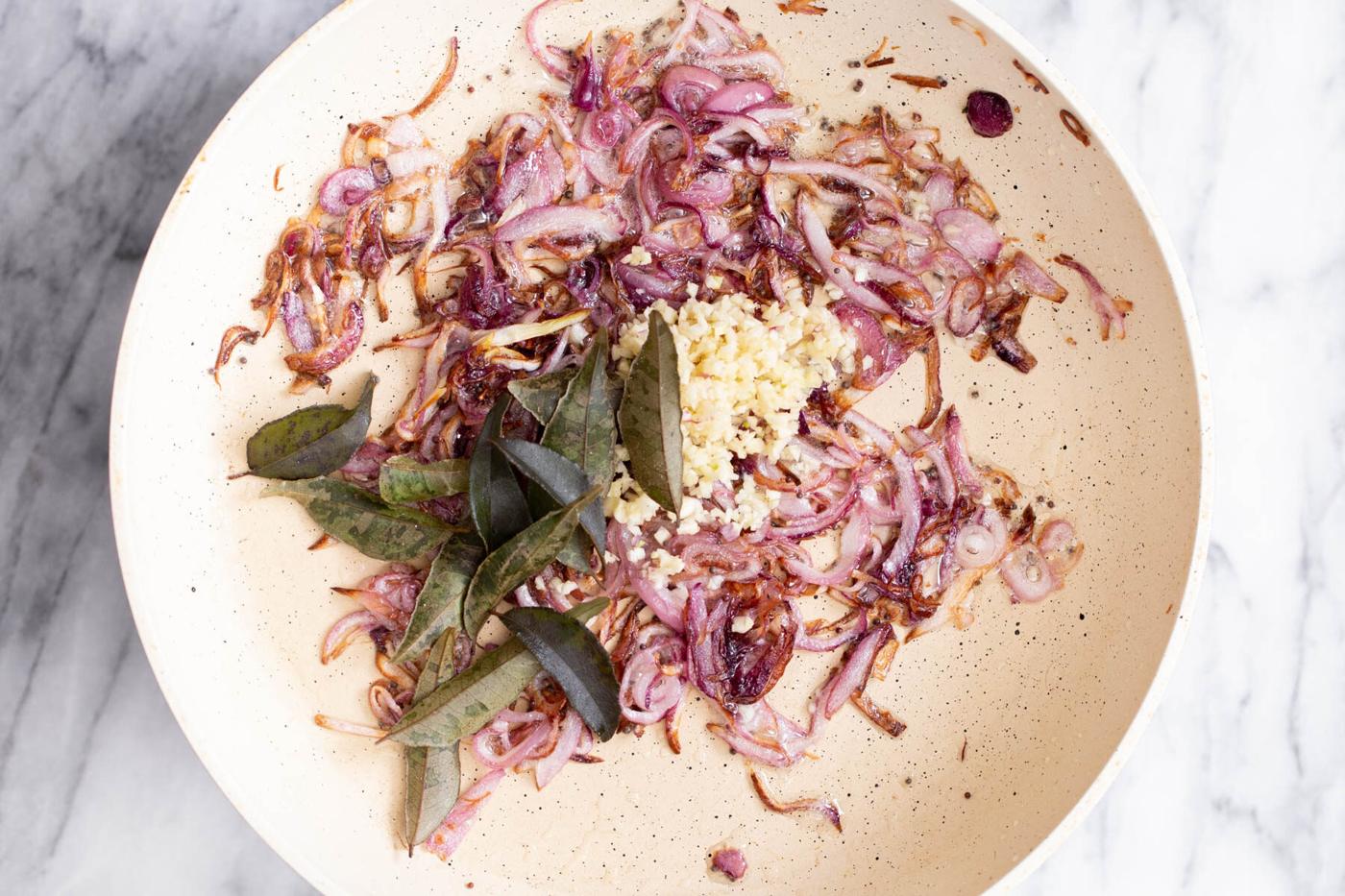 garlic and curry leaves being added to browned onions