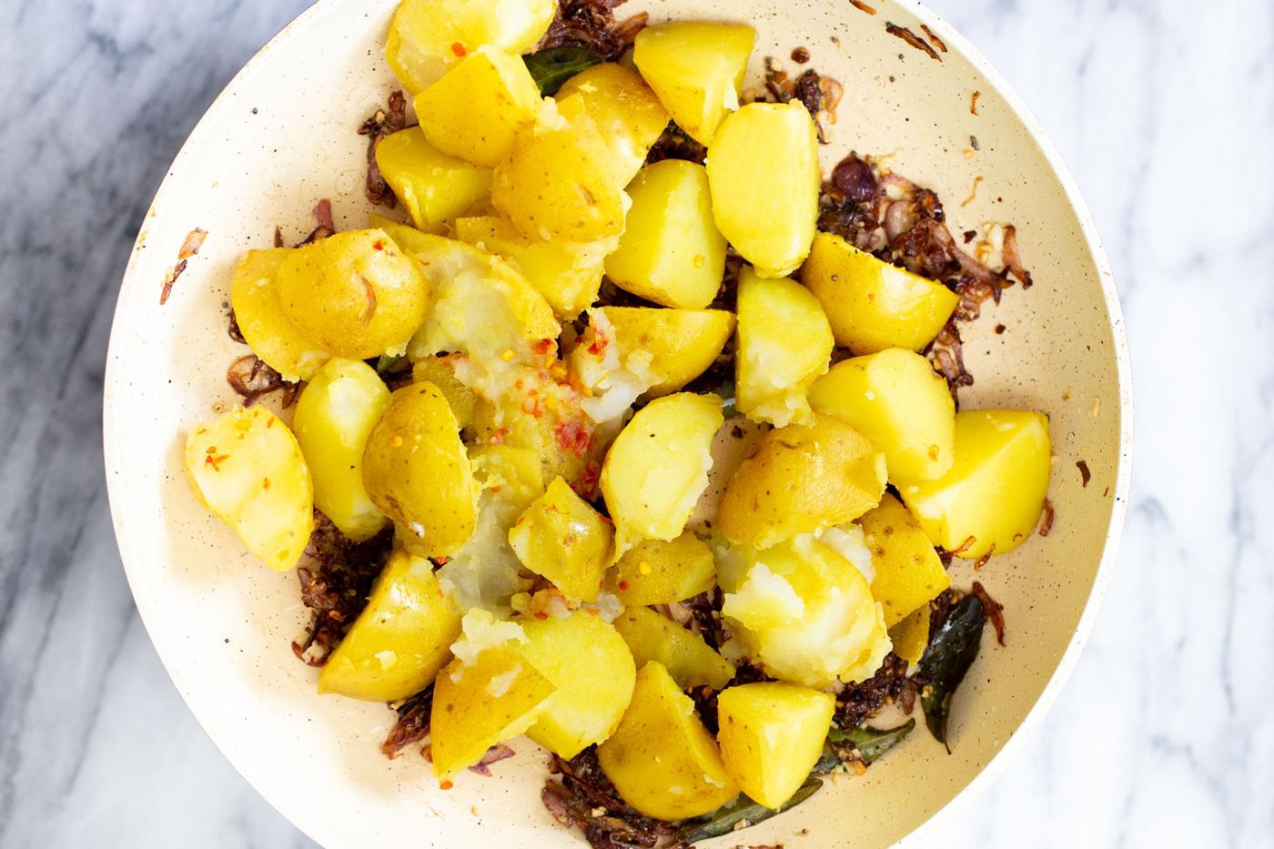boiled potatoes being added to sauteeing pan with fried onions and tempering