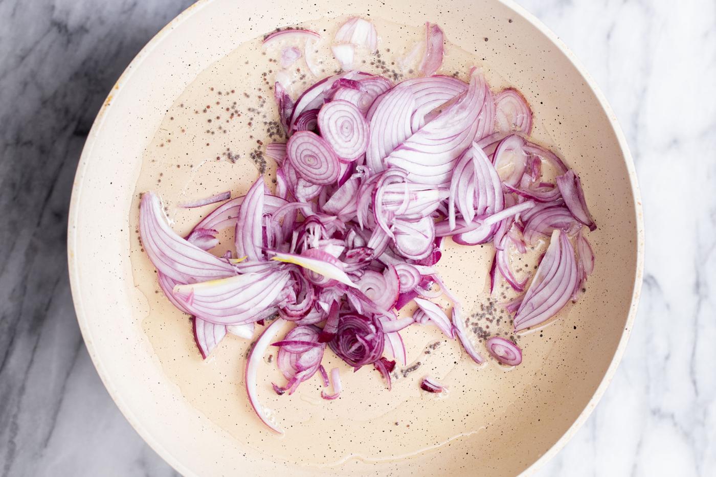 onions being added to frying pan with mustard seeds