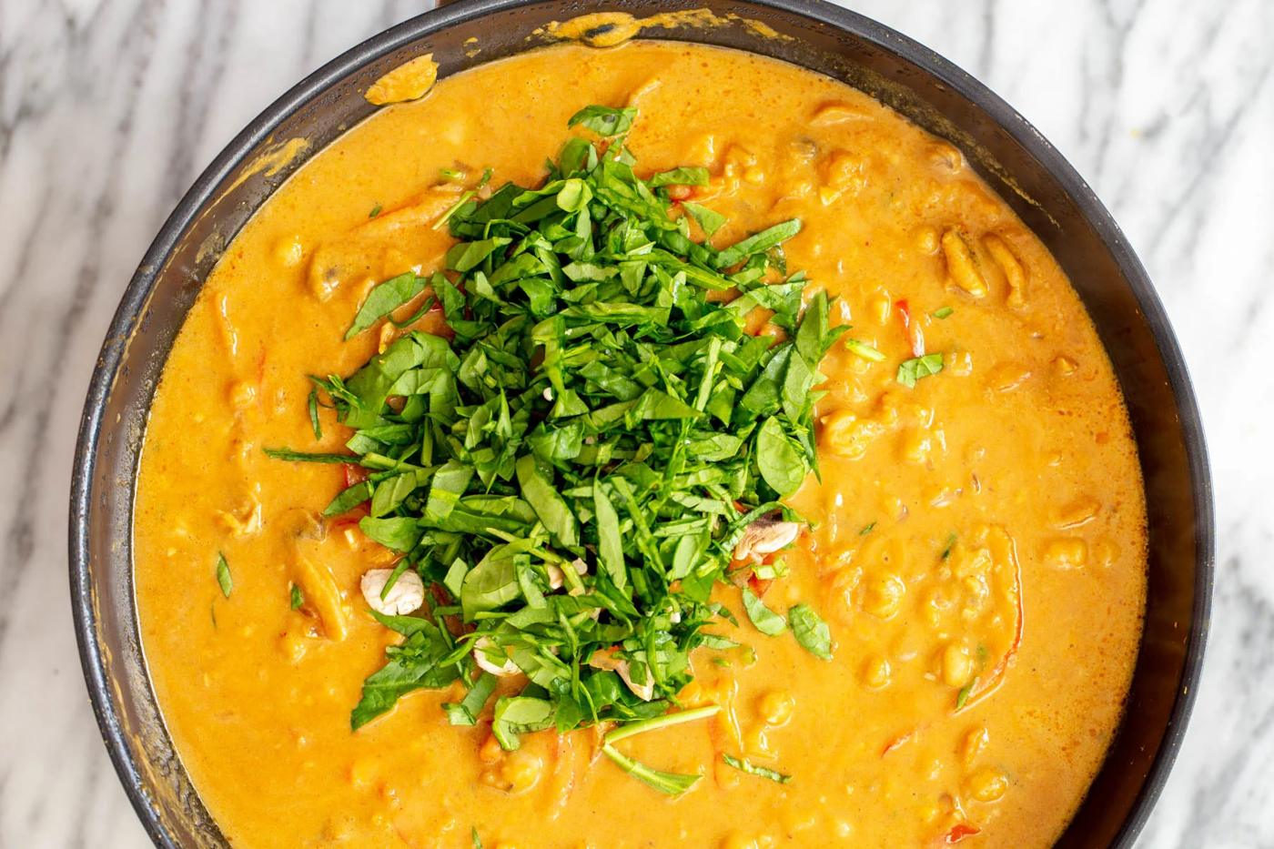 pumpkin chickpea curry being sprinkled with fresh herbs before serving