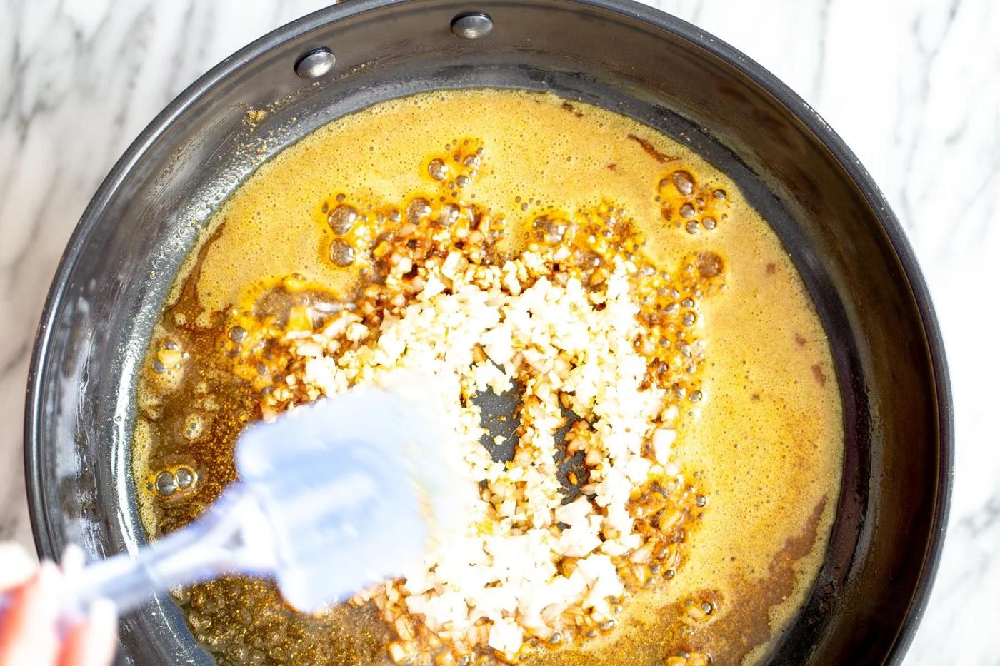 overhead shot of a skillet with fried spices and onion as base for curry recipe