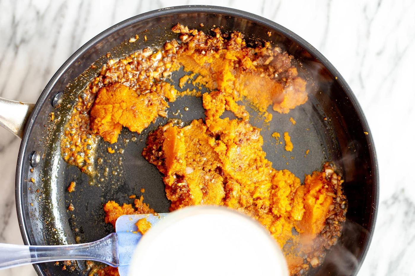 pumpkin puree being added to pan with tempered Indian spices