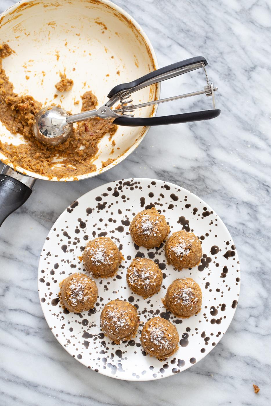 pumpkin pie energy balls on a white plate with cookie scoop in a skillet