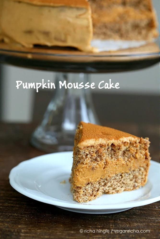 a slice of vegan pumpkin cake filled with dairy-free pumpkin mousse on a cake plate with a cake stand in the background