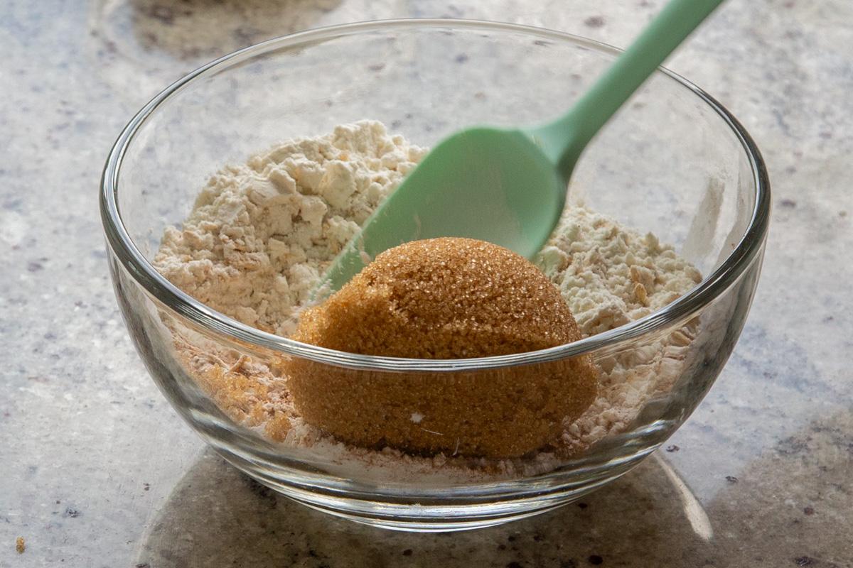adding brown sugar to the bowl of oats, flour, and spices