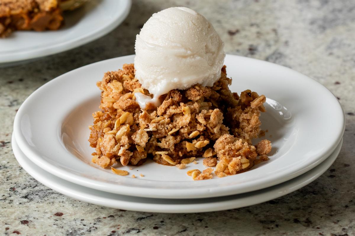 slice of pumpkin crisp on a white plate with ice cream on top