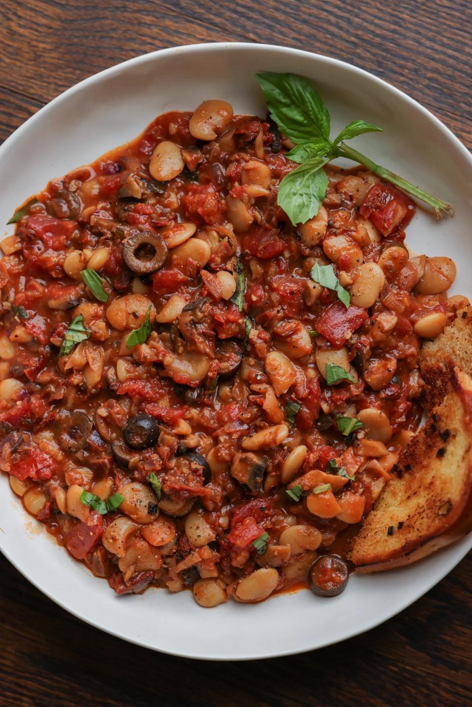close-up of puttanesca beans on a plate with garlic bread