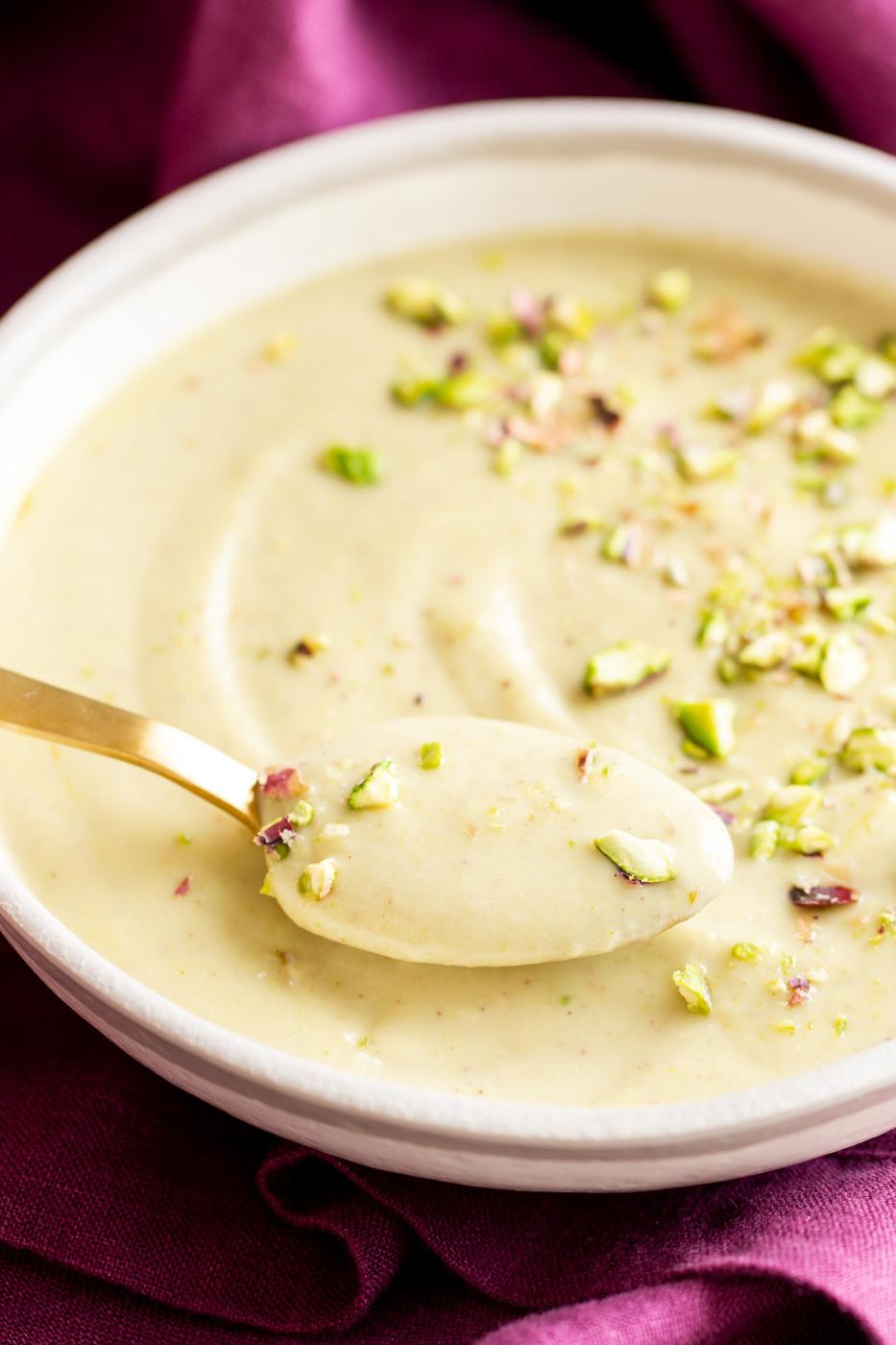a spoon being dipped in a bowl with vegan pudding rabri