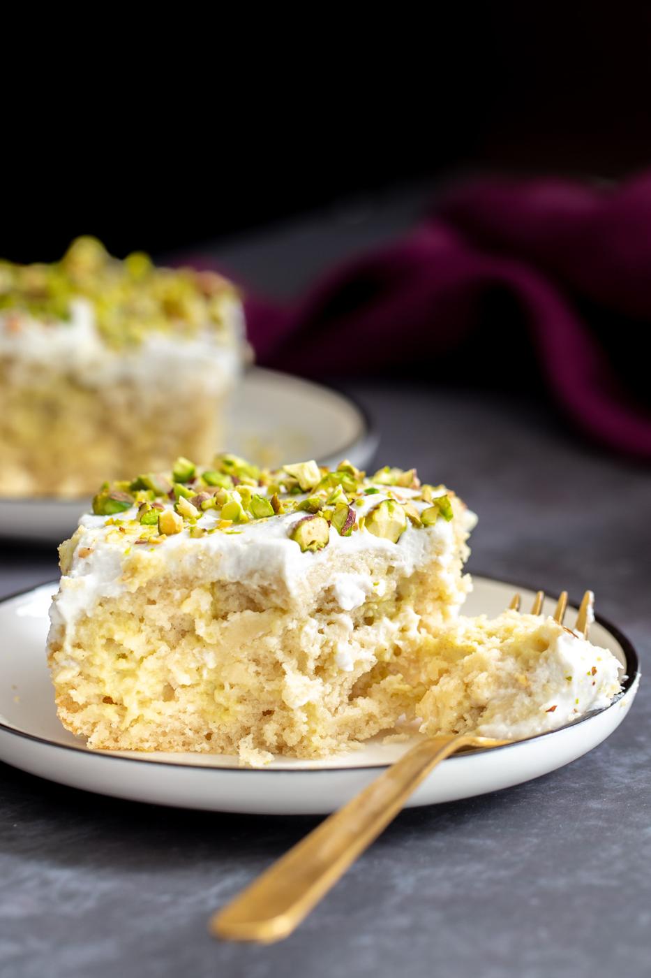 a half eaten piece of vegan ras malai tres leches cake with a golden fork on the side
