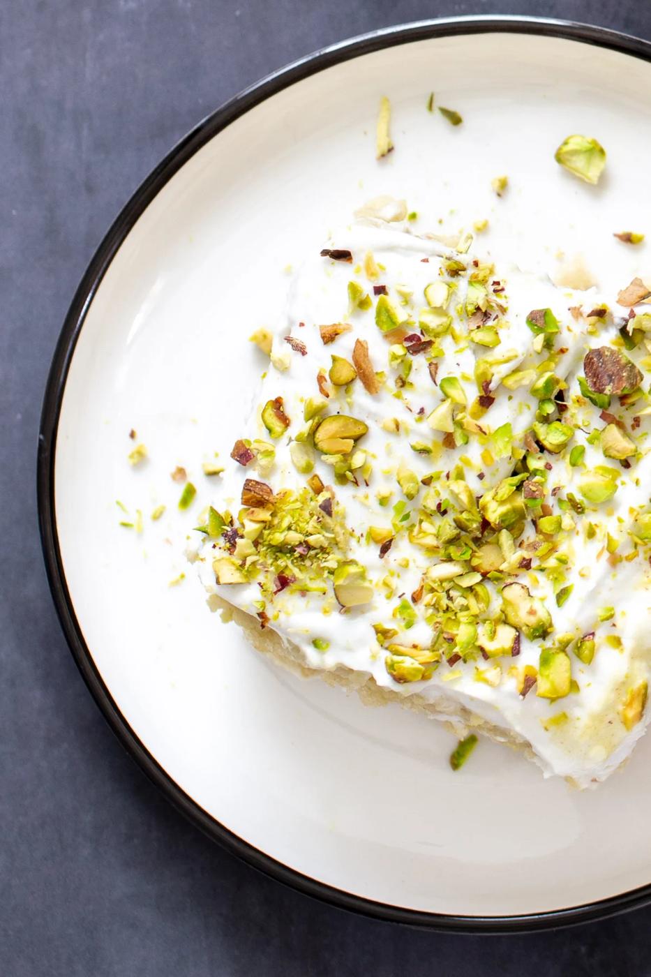 a slice of vegan ras malai tres leches sprinkled with pistachios served on a white plate