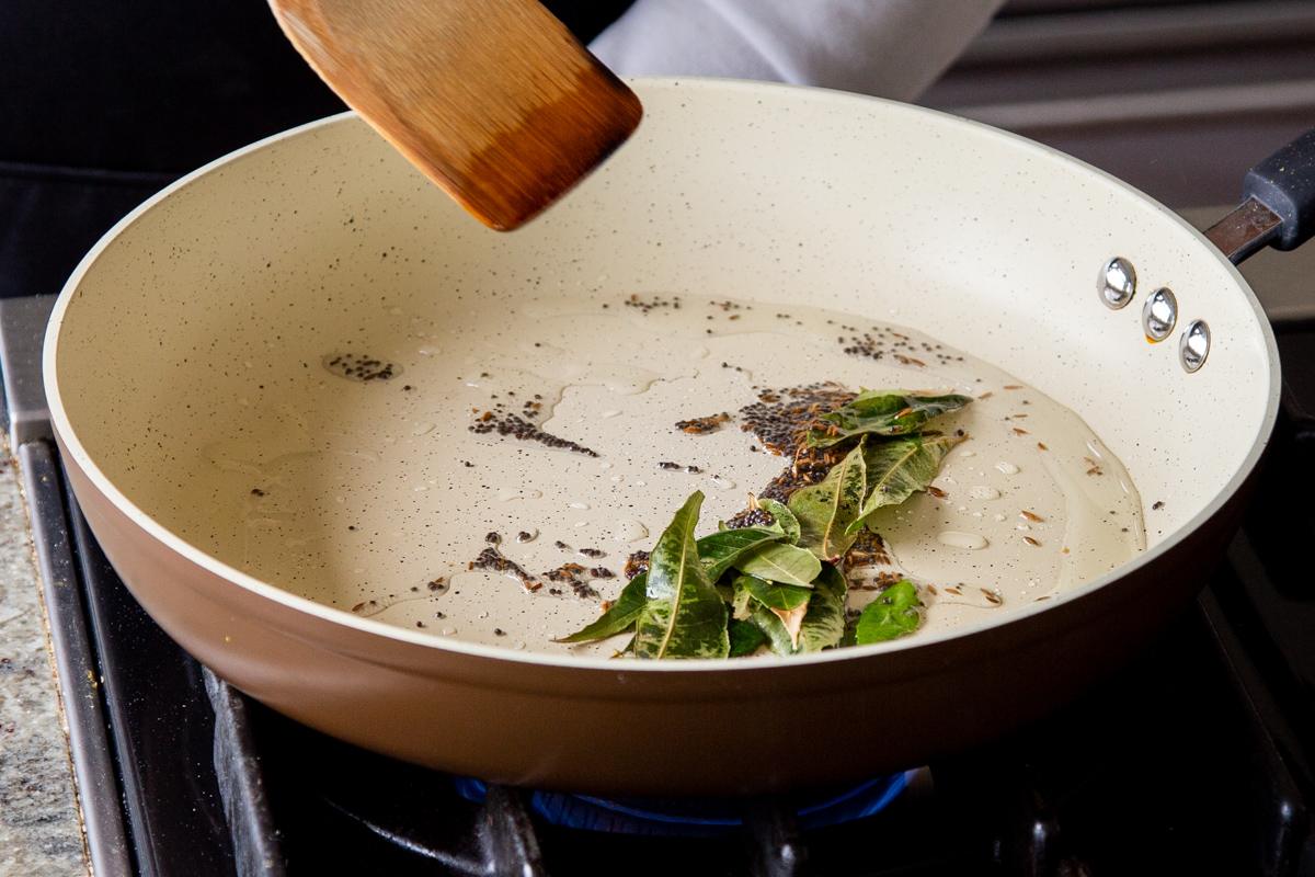 adding curry leaves to the pan of whole spices