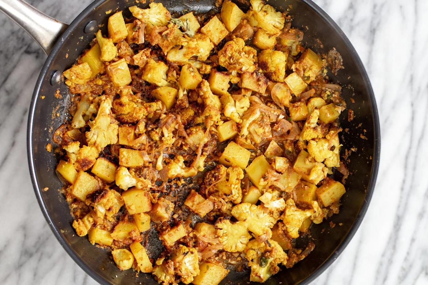 cauliflower and potato cubes being sauteed in onion garlic and tomato