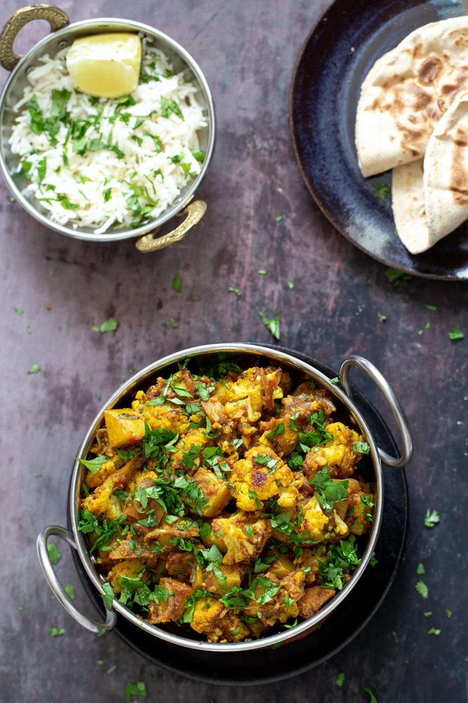 a small pot of rice and an indian dish with vegan aloo gobi on a wooden surface