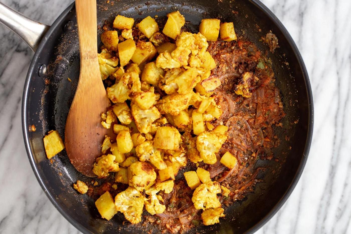 cauliflower and potato cubes being tossed with sauteed spices