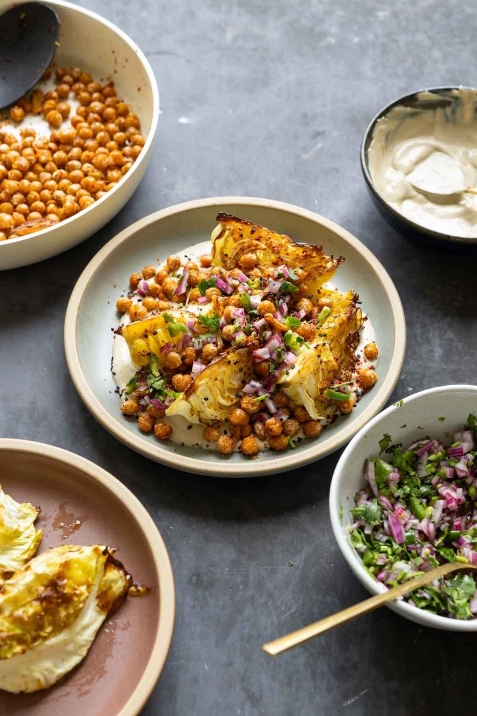 roasted cabbage wedges on a bed of tahini sauce with crispy chickpeas and gremolata surrounded by bowls of each component