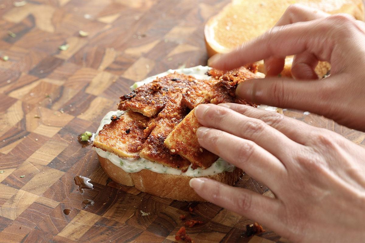 adding the yogurt sauce and coconut tofu to the sandwich