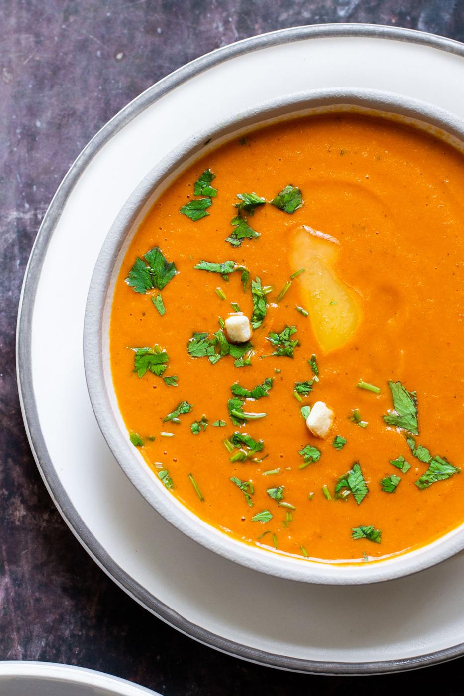 a bowl of vegan roasted tomato soup served sprinkled with chopped herbs and a drizzle of olive oil