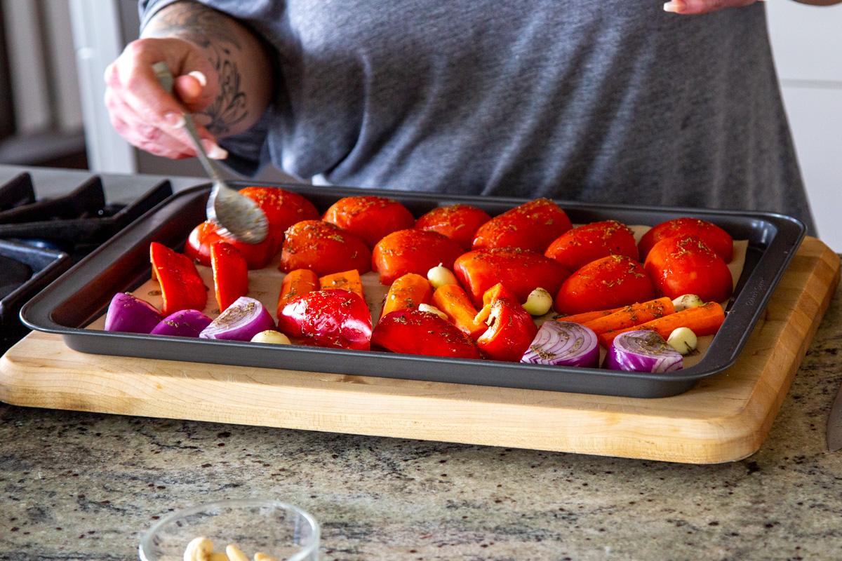 bell pepper, tomatoes and onion on a baking sheet being drizzled with seasoned oil