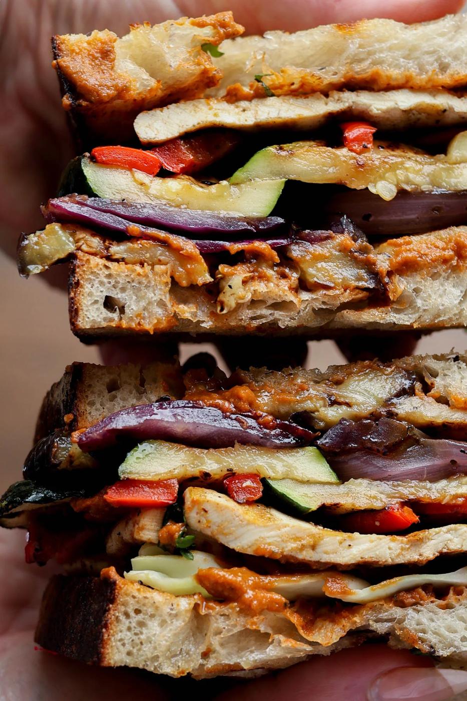 hands holding a sliced grilled veggie sandwich