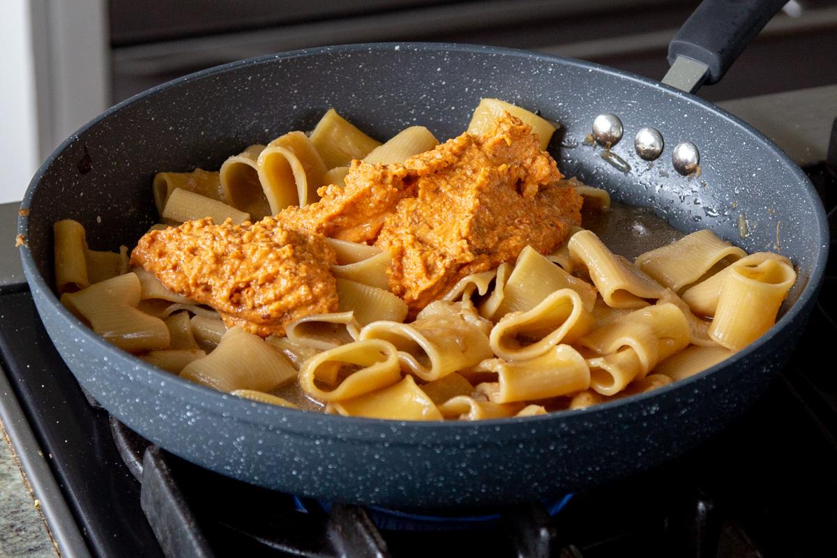 adding romesco sauce to the cooked pasta in the skillet