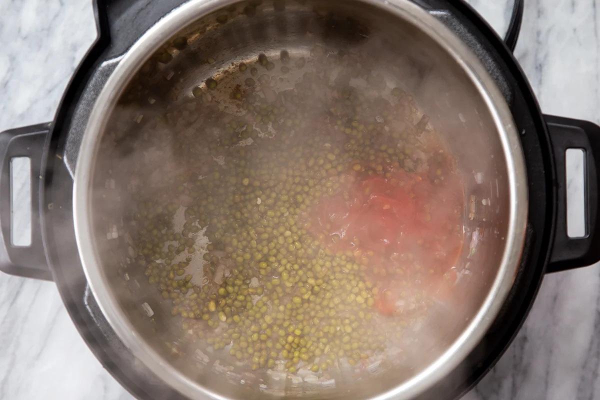 tomatoes and mung beans being added to sauteed onions to make dal