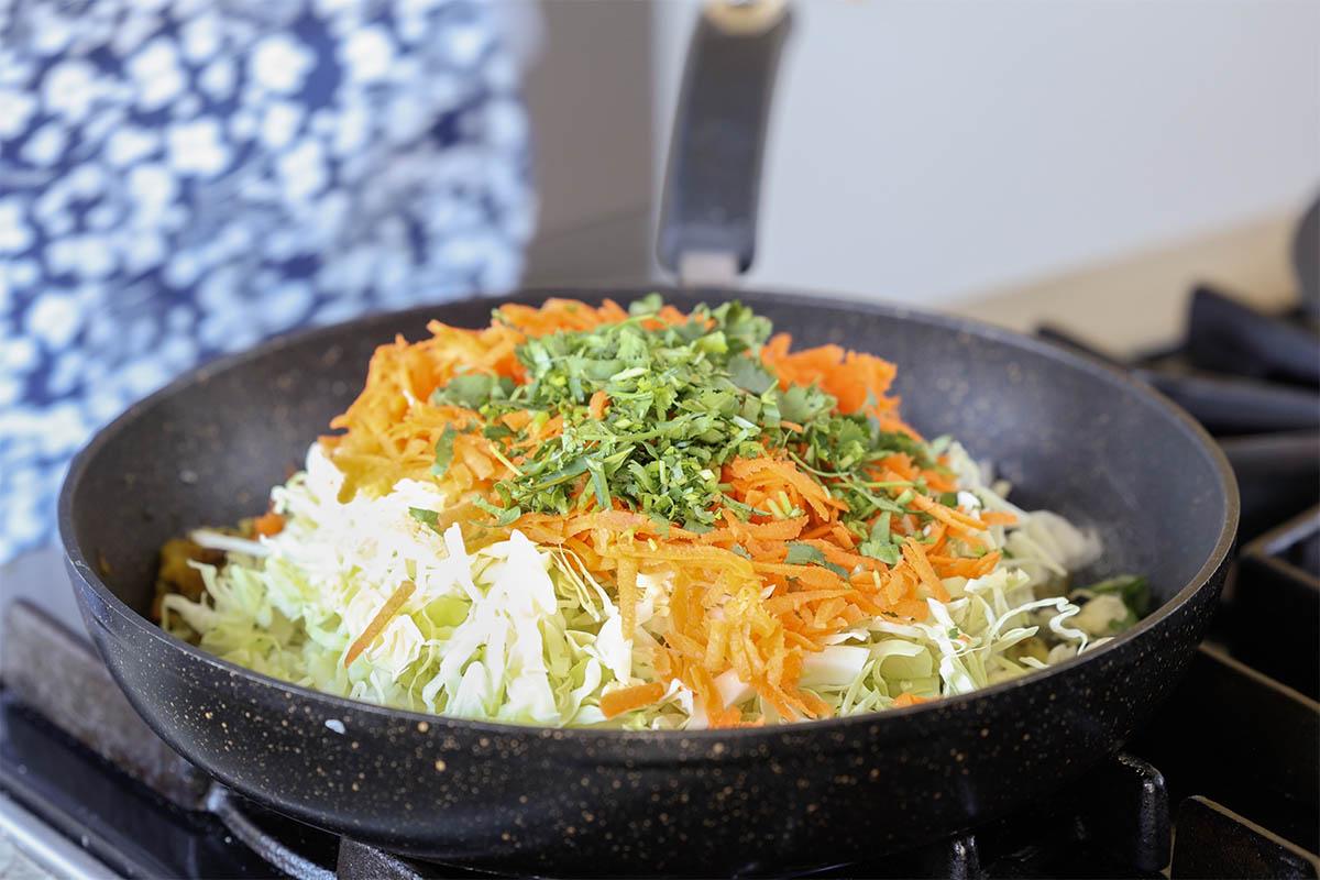adding cabbage, carrots, and cilantro to the pan