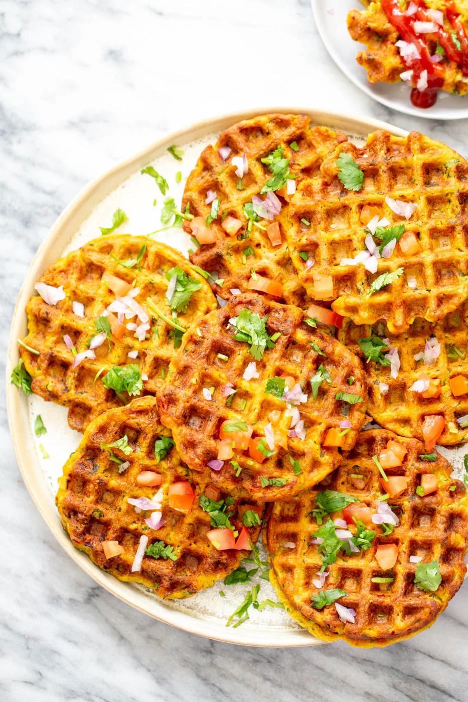 overhead shot of a plate of crispy pakora chickpea flour waffles topped with fresh onions and herbs