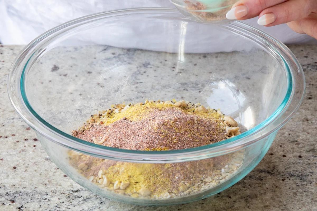 adding spices to the bowl of oats, nuts, and almond flour