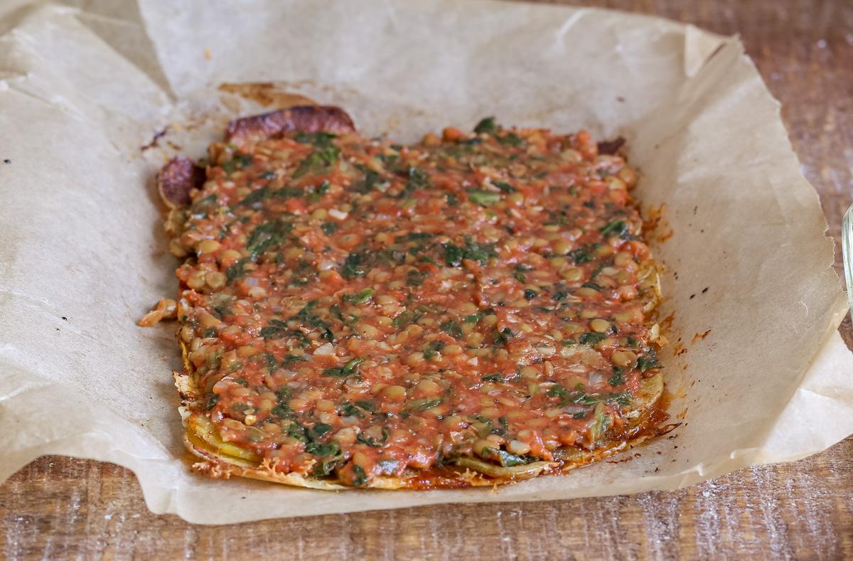 savory lentil sausage filling being spread over baked vegan scalloped potatoes