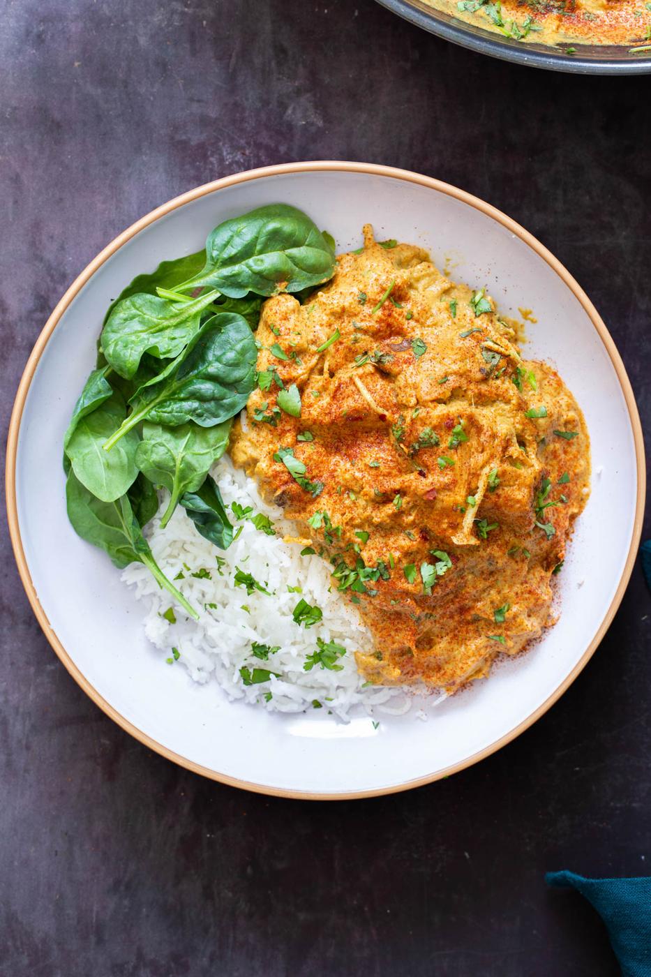 a serving of vegan chicken korma with jackfruit on a white plate served with rice and spinach
