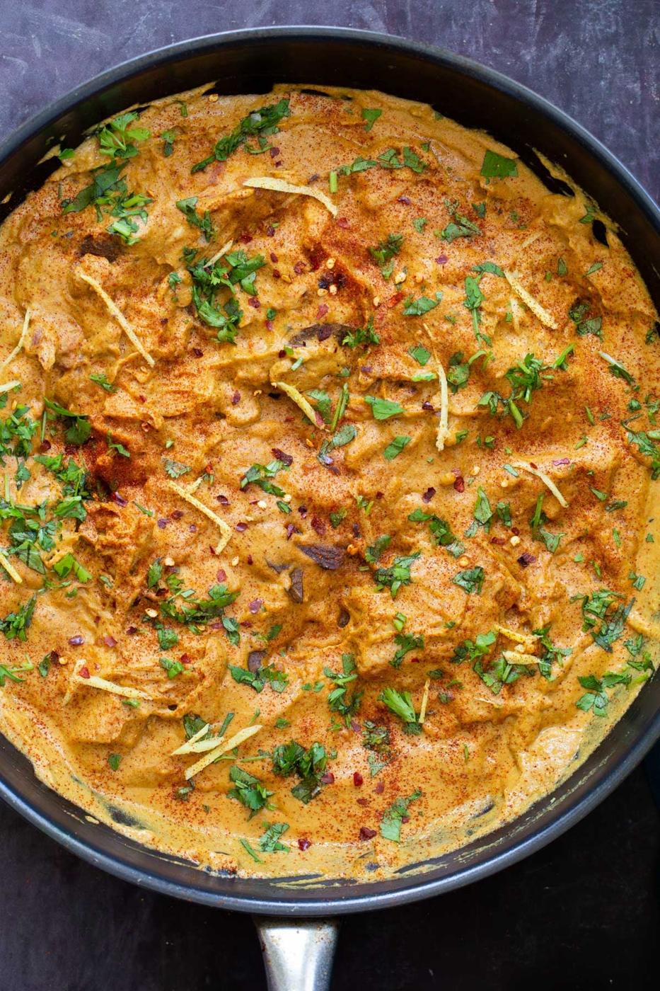 a black skillet with vegan jackfruit korma sprinkled with herbs