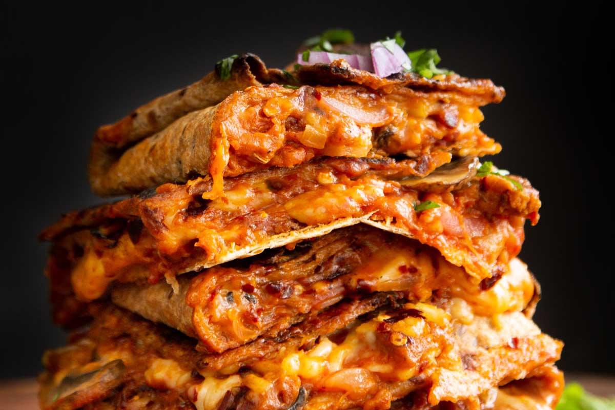stack of vegan pizza quesadilla slices on a wooden cutting board