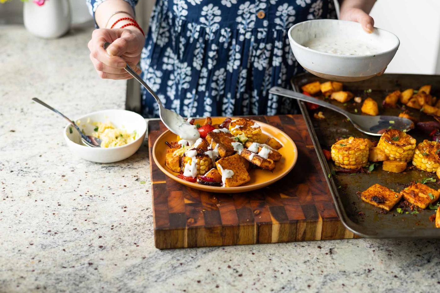 adding yogurt sauce to the peri-peri tofu and vegetables on a plate