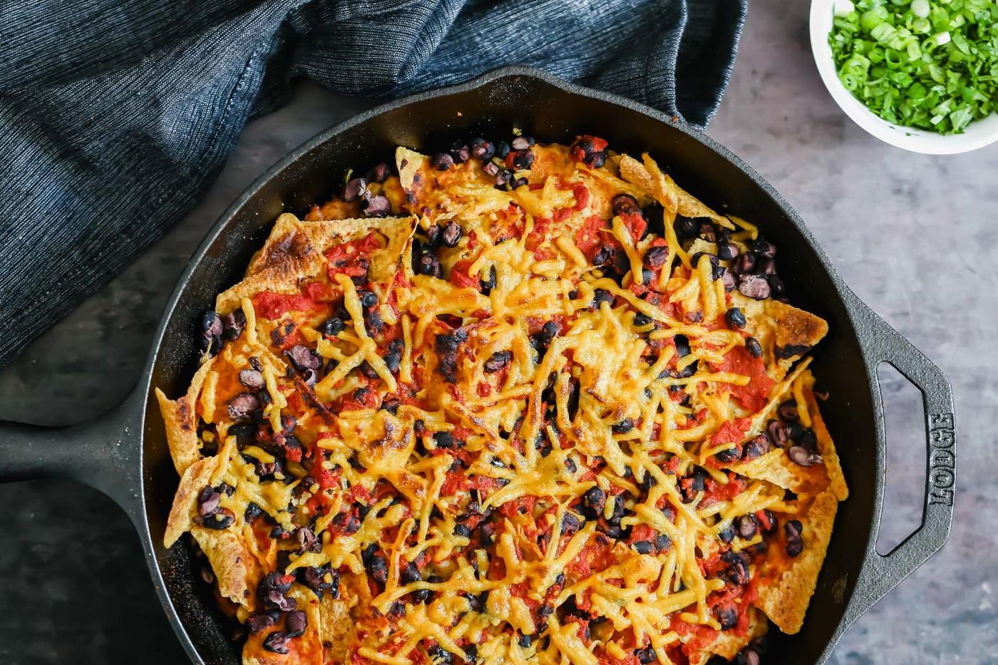 vegan skillet enchiladas with red sauce and black beans next to a dish with green onions