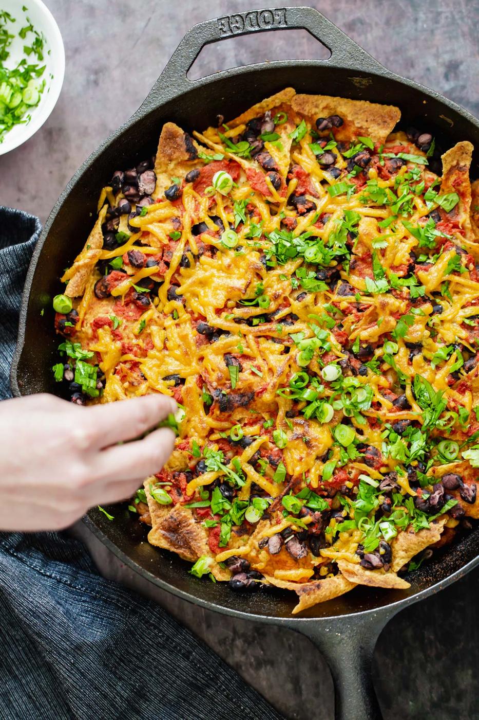 a hand reaching for a serving of vegan skillet enchiladas with black beans