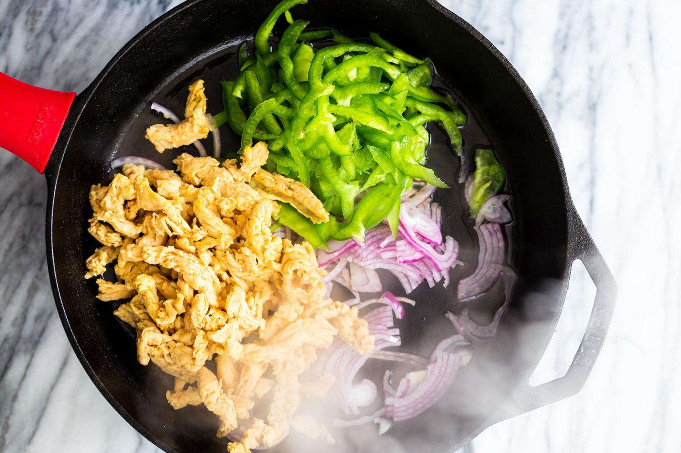 onions bell peppers and soy curls sauteeing in a black skillet